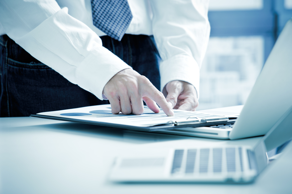 person in white shirt pointing at cash flow document on a clipboard while standing at their desk