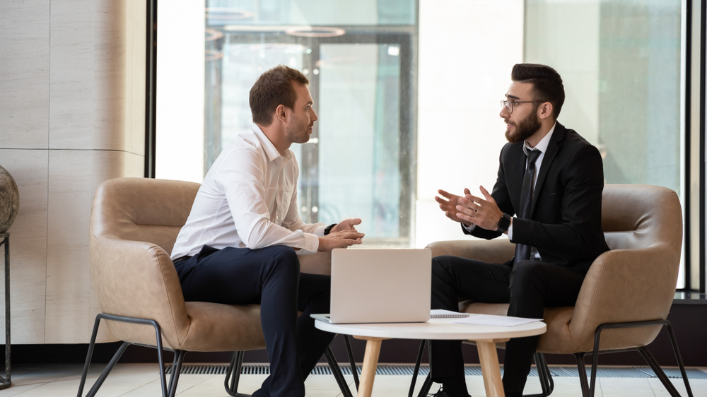 two business people having a conversation at a small table with a laptop on top of it